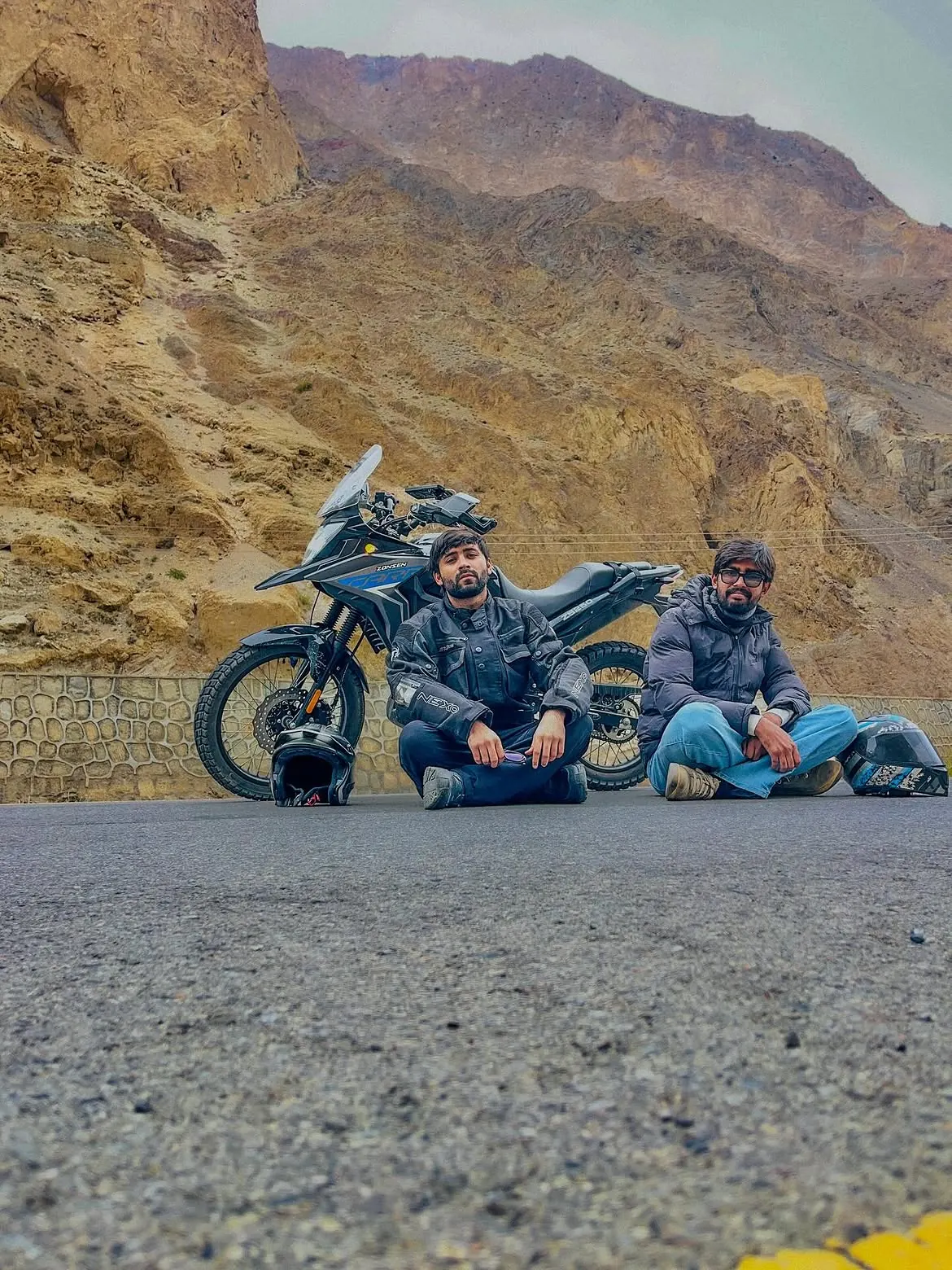 Riders resting beside a motorcycle in mountain terrain